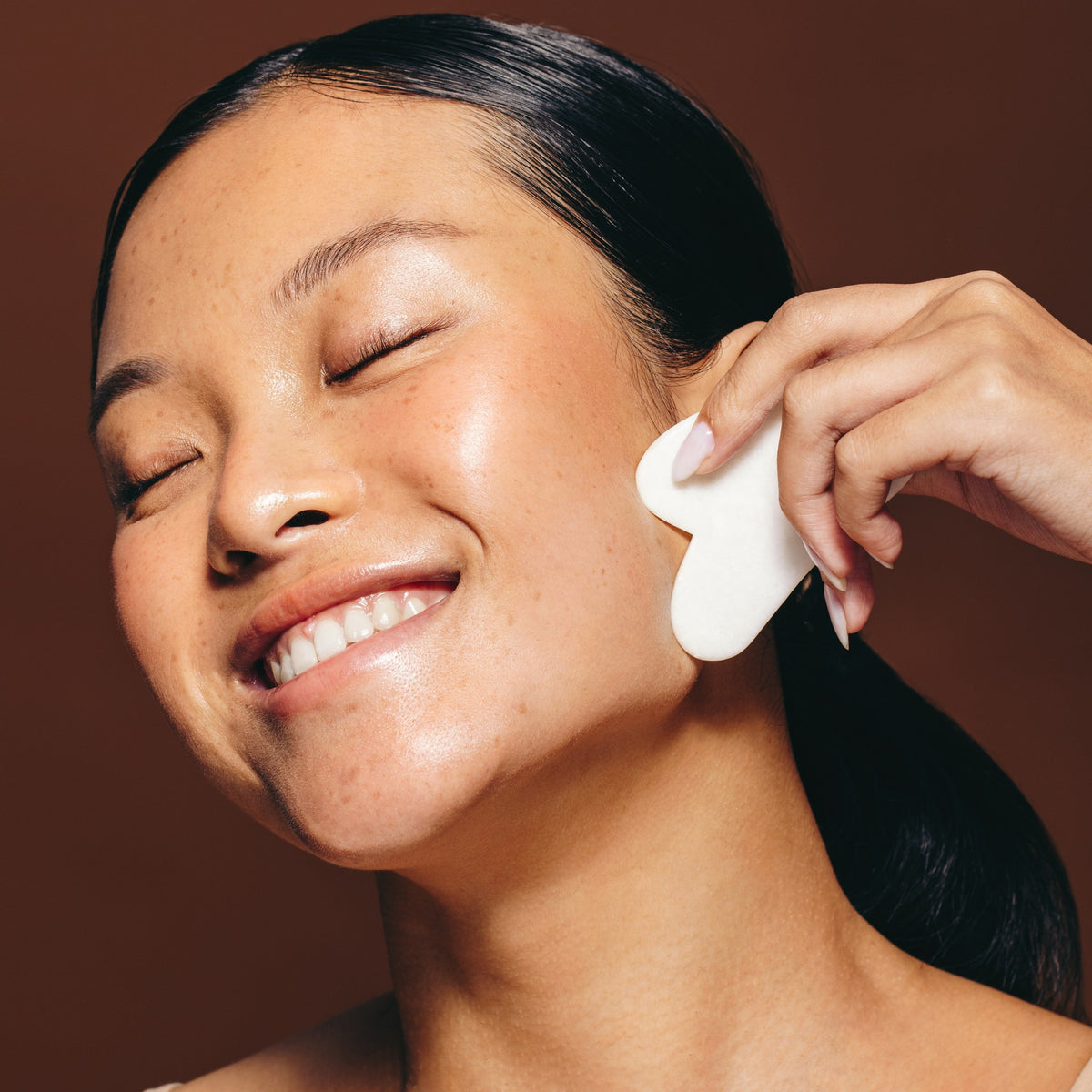 Woman using a gua sha tool along her cheek during a facial treatment