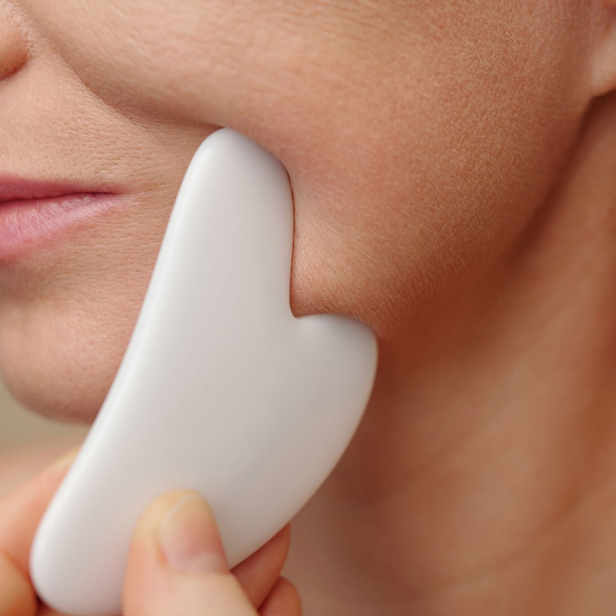 Close-up of a gua sha tool drawn along the jawline and neck