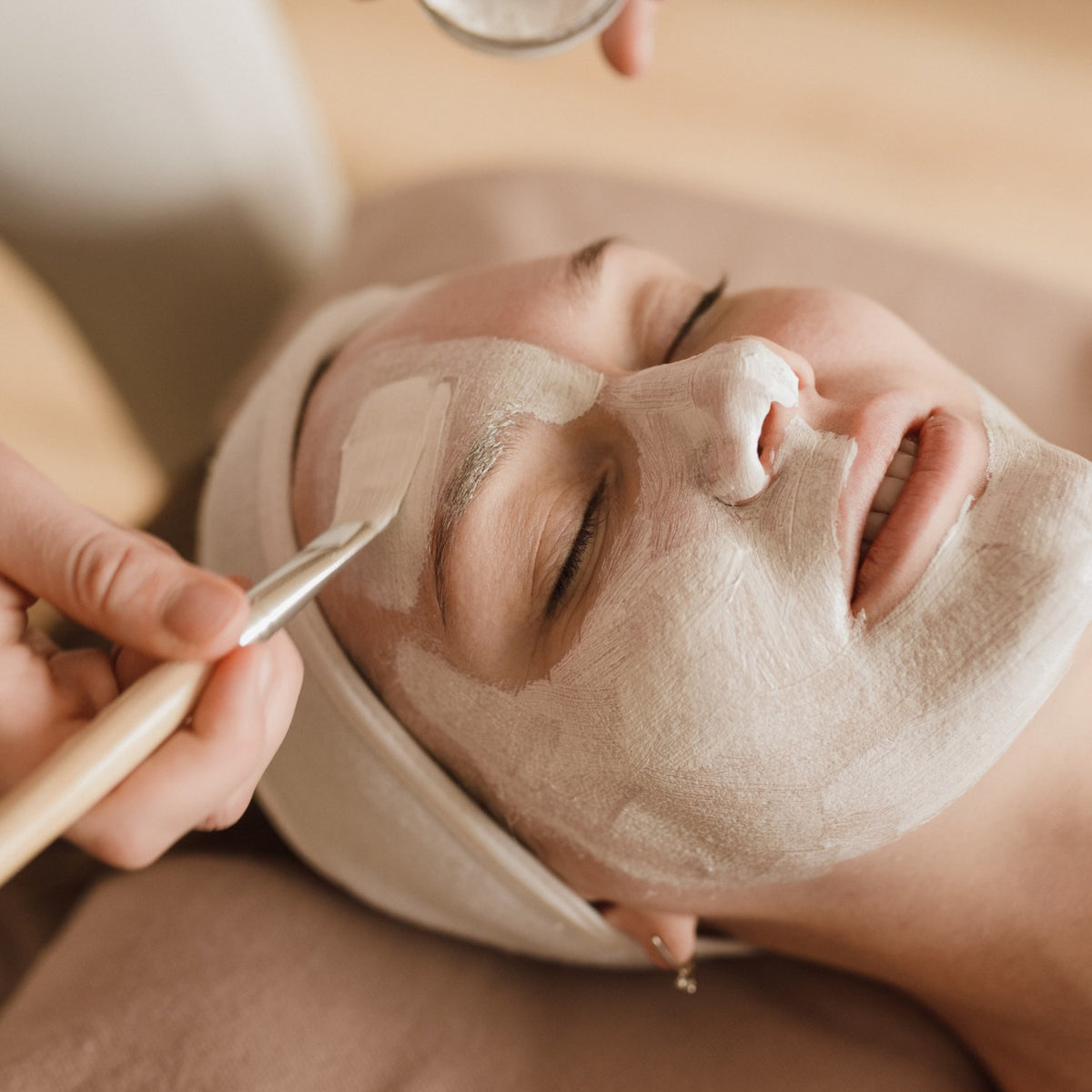 Herbal clay mask being applied to a client's face with a spatula during a treatment