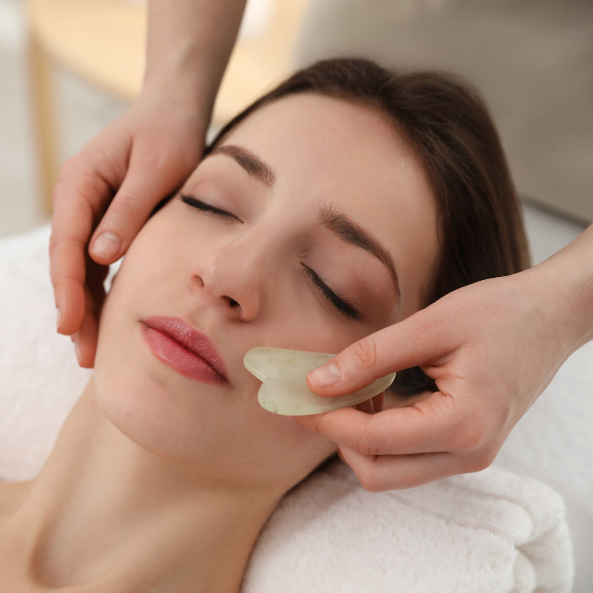 Jade gua sha stone used across the cheek during a Chinese medicine facial treatment